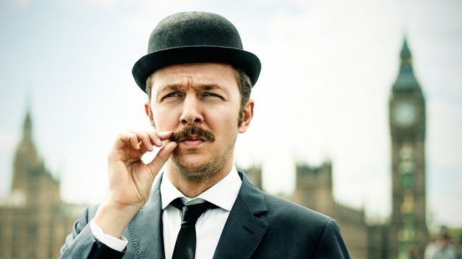 ビッグベンを背景に、ひげを気にするイギリス人男性