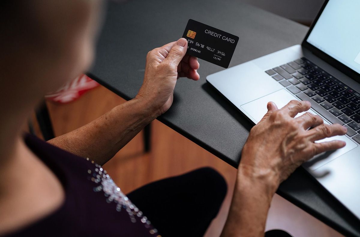 クレジットカードを片手にパソコンを使う高齢者