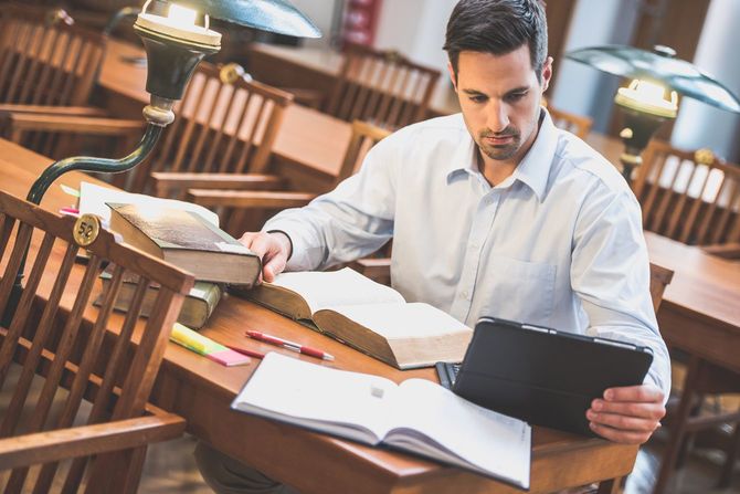 図書館でタブレットと書籍を広げる男性
