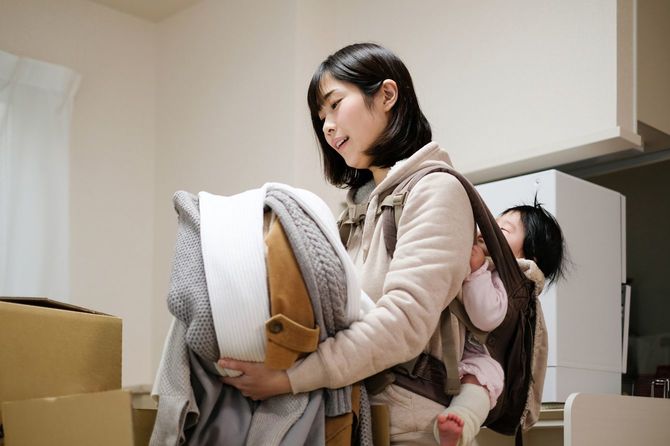 赤ちゃんを負ぶって引っ越しの準備を進める母親