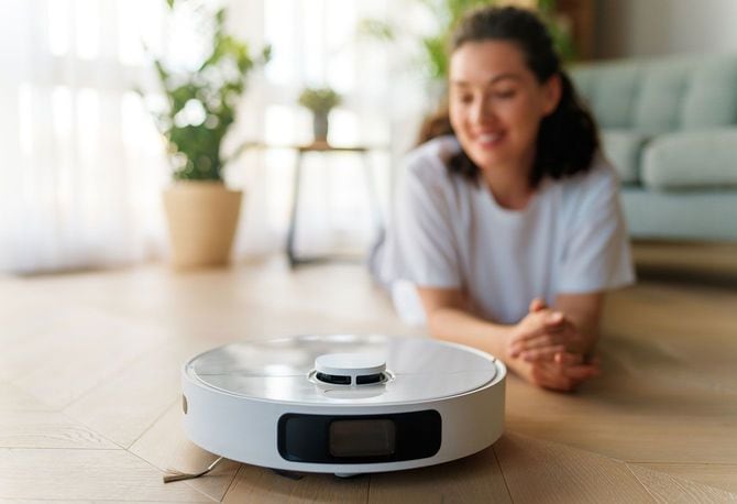 リビングの床で稼働するロボット掃除機と、それを見ている女性