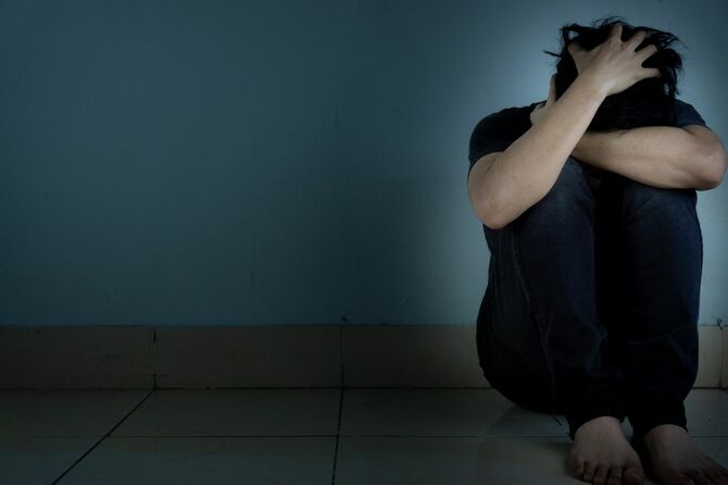 ひざを抱えて床に座り込んで苦悩している男性