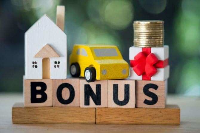 ボーナスと書かれた木製ブロックの上にミニチュアカーとおもちゃの家
