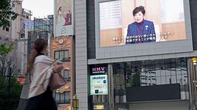 小池百合子都知事の発表を示すスクリーンを見あげる女性