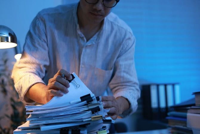 薄暗い部屋で書類の山を整理するビジネスマン