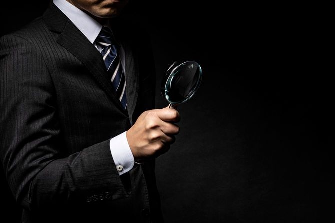 手に虫眼鏡をもちスーツを着た男