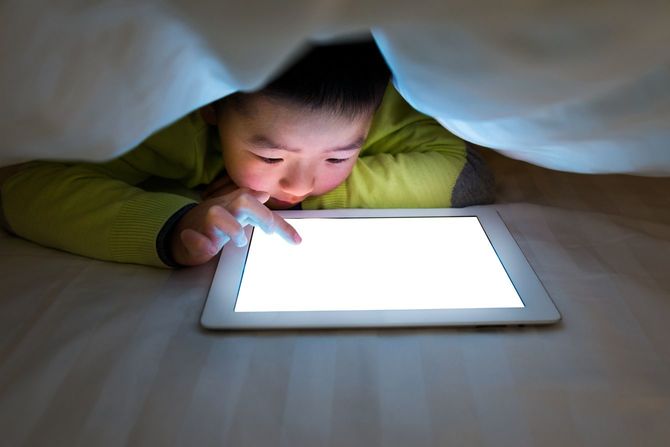 布団の中でタブレットを見ている少年