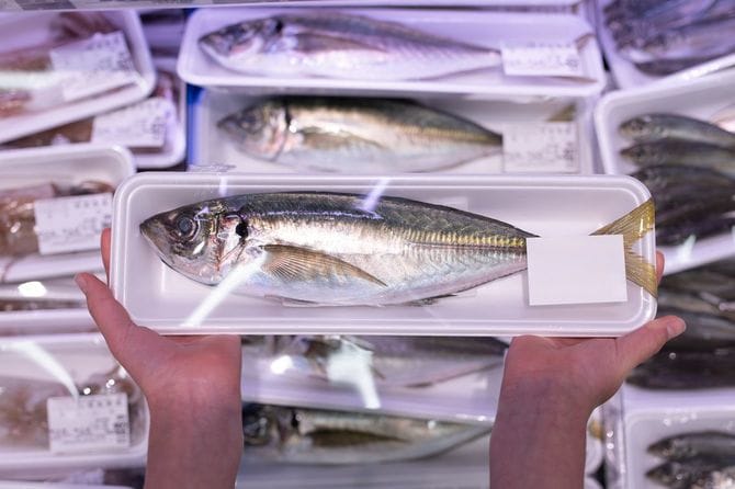 スーパーの鮮魚売り場で、パック詰めのアジを手にしている