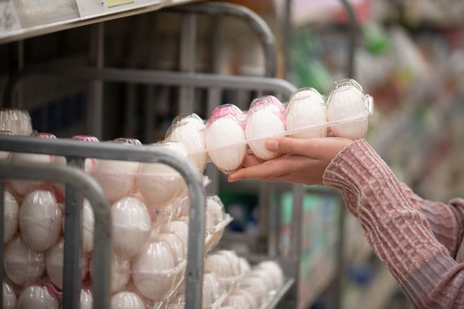 スーパーで卵10玉入りのパックを手に取っている女性の手元