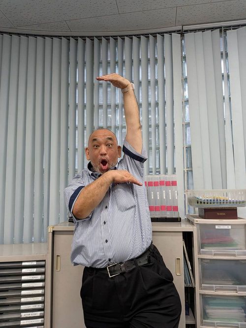 勤務先の進学塾でポーズをとって撮影に応じる現在の山田さん
