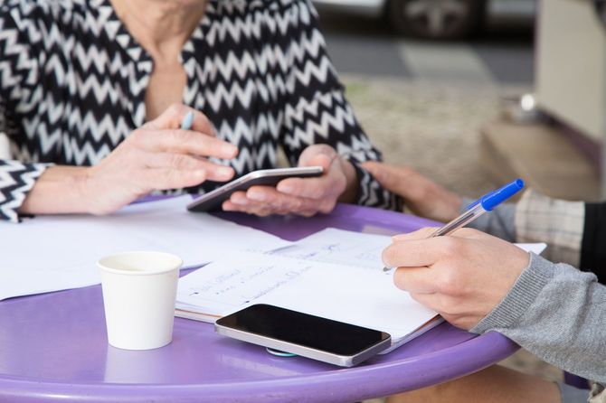 カフェのテーブルで、スマホにメモを取りながら会話する2人