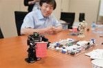 背丈が16.5cmのアイソボットに対し、紙コップは胸の高さ程度。ロボットの動く原理は、からくり人形とも共通点が。