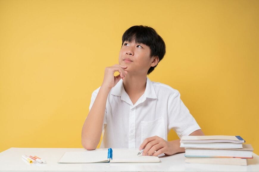 本とノートを持って机に座って問題を熟考する学生