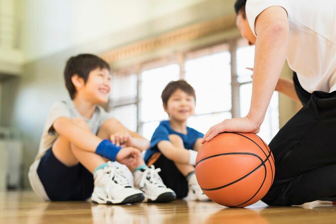 バスケットボールコートでコーチと練習する少年たち