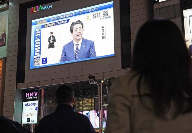 緊急事態宣言発令後に行われた安倍晋三首相(当時)の記者会見を映す街頭ビジョンと足を止めて見る人々