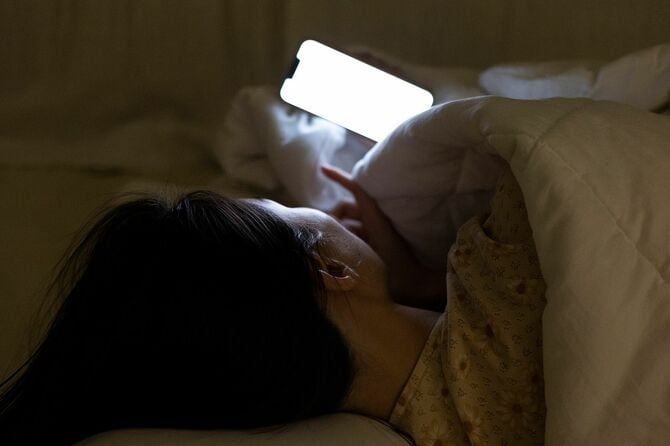 寝ながらスマホを眺める女性