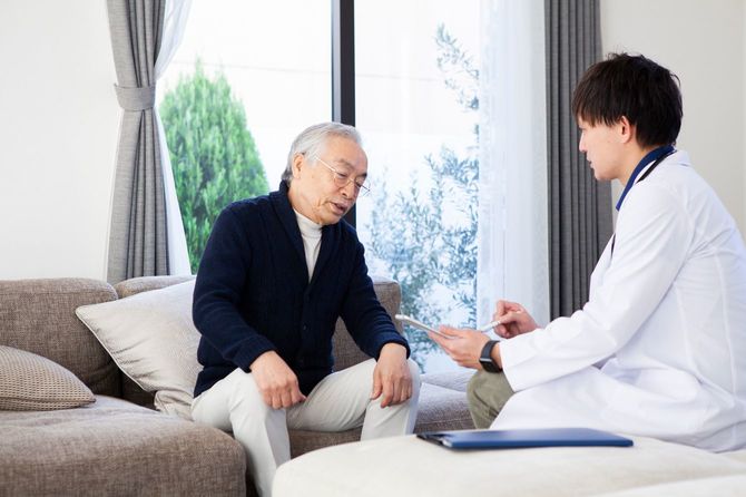 自宅の居間で訪問医の診察を受けるシニア男性