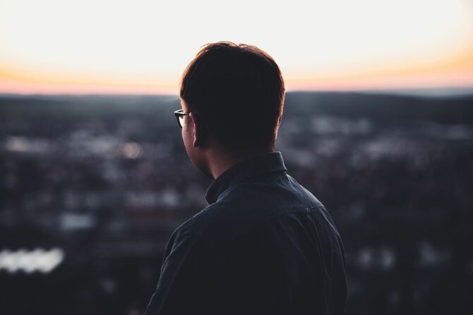 丘の上から暮れなずむ町を見下ろしている男性