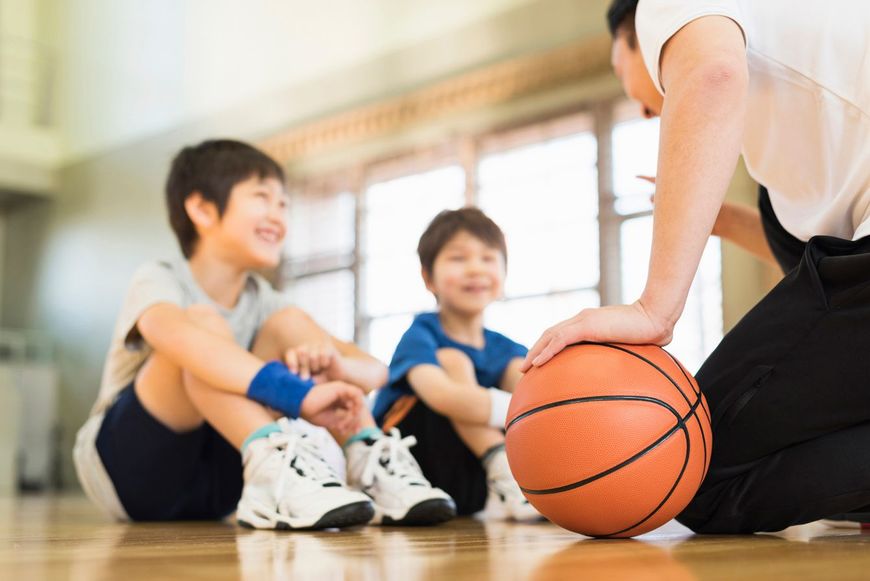 バスケットボールコートでコーチと練習する少年たち