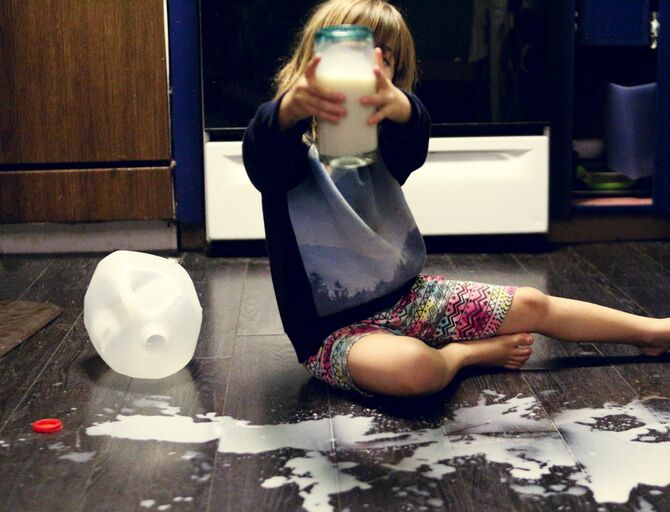 ミルクのボトルの中身を床にこぼして手にミルクの入ったビンを持つ女の子