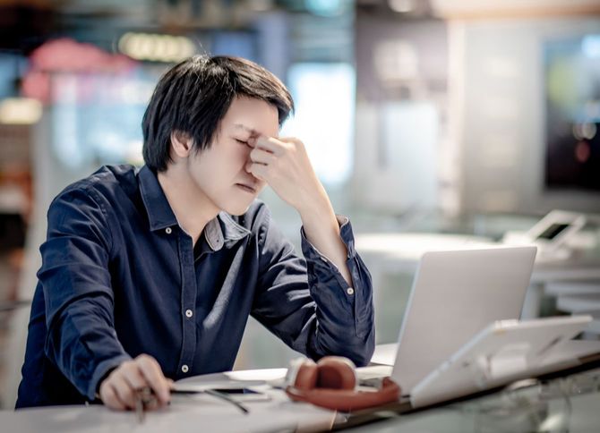 ラップトップで作業中、ストレスを感じて眉間をつまむ男性