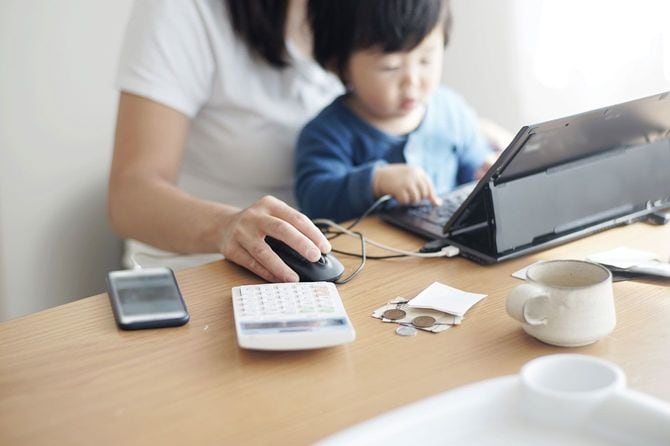 家で子どもを膝の上にのせて仕事をする母親