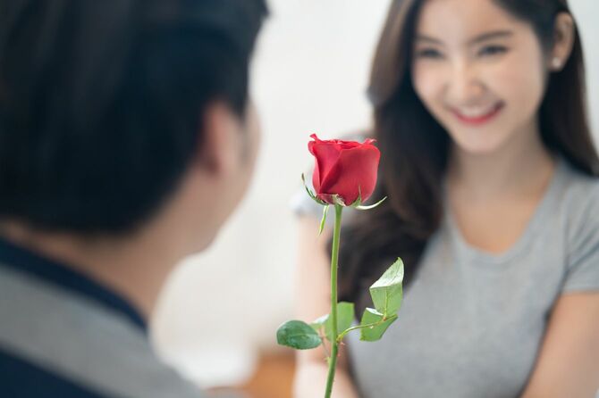女性に赤いバラの花をあげるアジアの若者