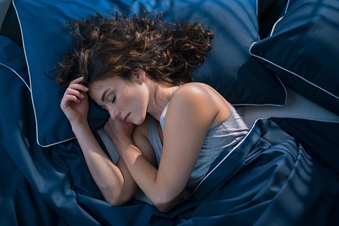 深いブルーの寝具で統一されたベッドで眠る若い女性