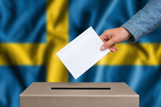 一票を投じる手元の背景にスウェーデン国旗