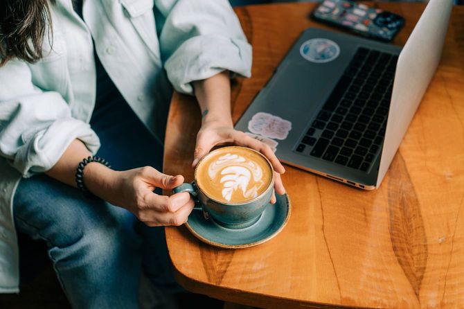 カプチーノの入った大きなマグカップを持っている人
