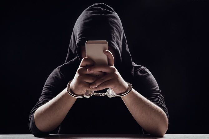 手錠をかけられたままスマートフォンを操作している黒い服の男