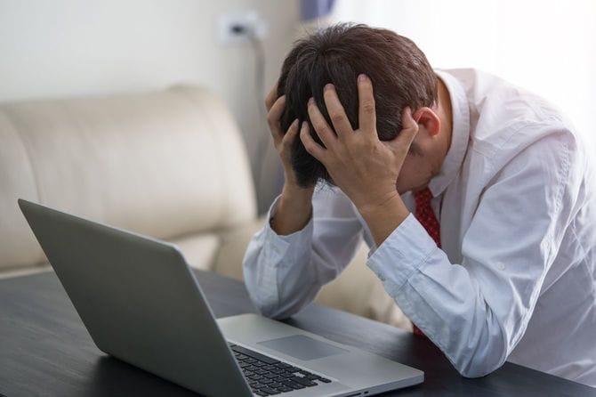 ノートパソコンの前で、頭を抱えている男性