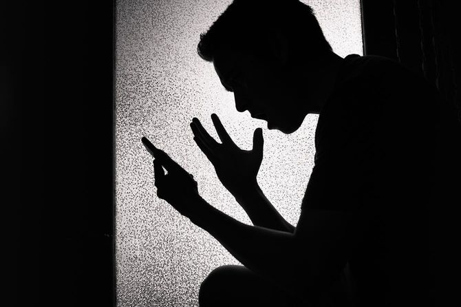 感情的になって携帯電話の画面を見ている人物のシルエット