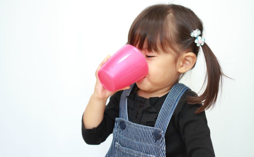 3歳の女の子がコップで水を飲んでいる