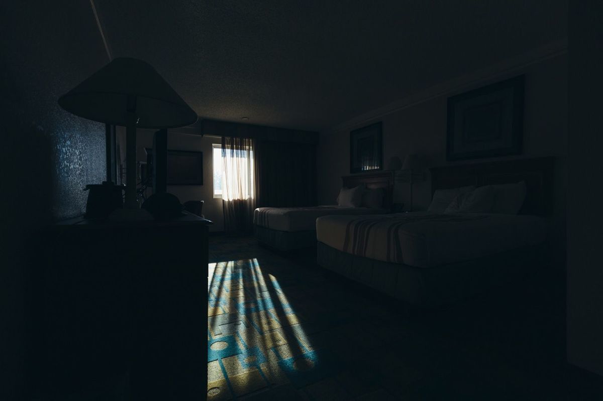 消灯されて窓から光が差し込む安価なビジネスホテルの部屋