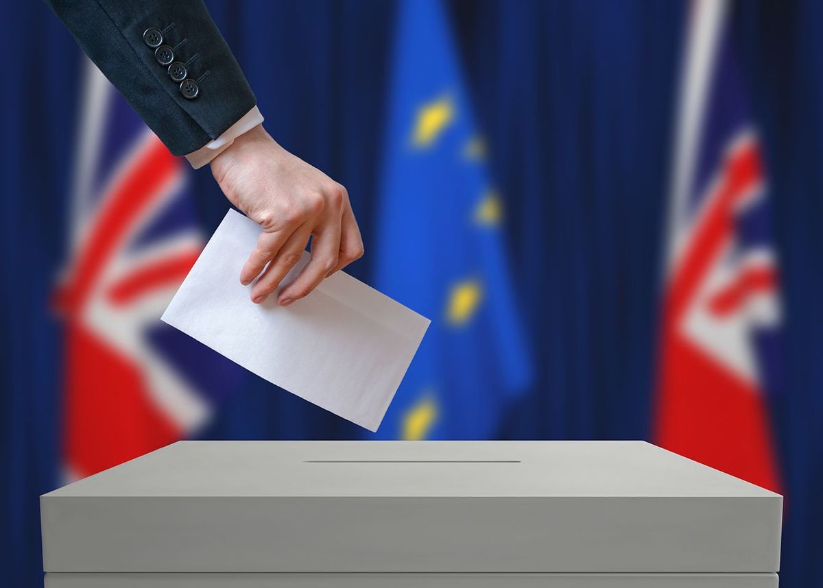 イギリスの選挙または国民投票。投票者は投票票の上に封筒を手に持っています。背景に英国と欧州連合の旗。