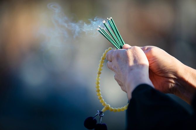 火のついた線香と数珠を手にするシニア女性