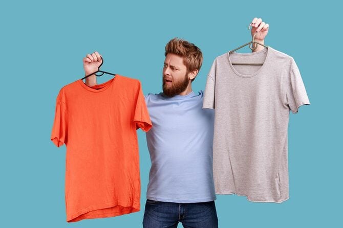 灰色とオレンジ色のTシャツを着た2つのハンガーを持って顔をしかめている男