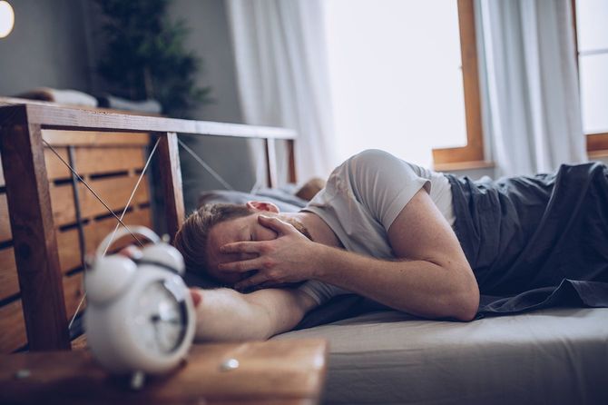 目覚まし時計を止める不快そうな男性