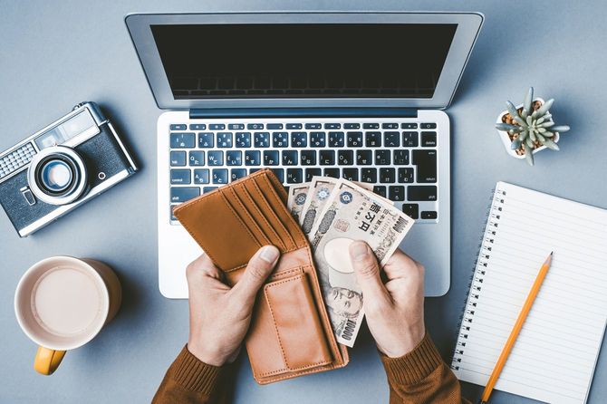 ノートパソコンの前で財布から複数の一万円札を取り出す人の手元