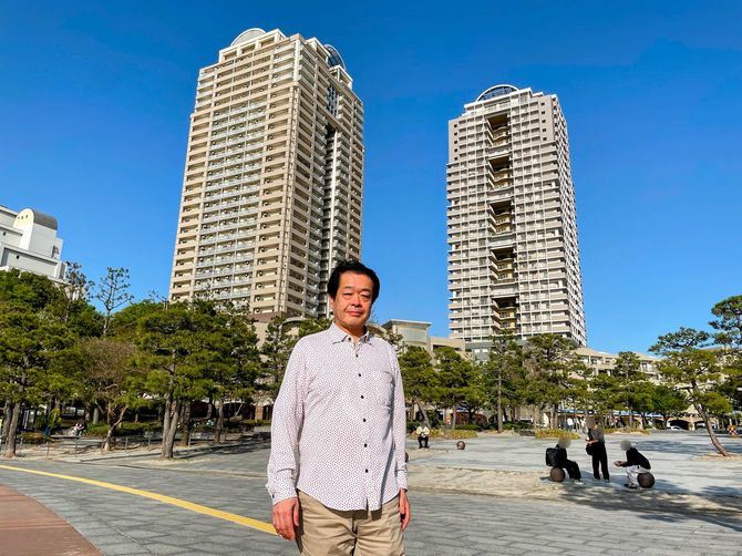 安田功さん。後ろに建っているのが現在住んでいる賃貸マンション