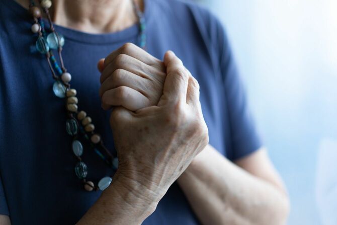 胸の前で自分の手を握る高齢女性