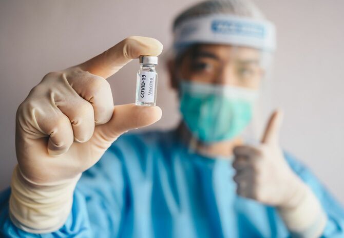 新型コロナウイルスワクチンを手に、サムズアップする医療従事者