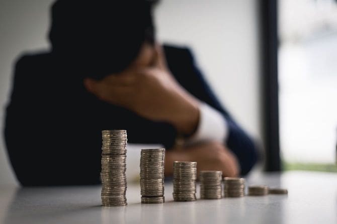 積み重ねたコインを前に頭を抱える男性