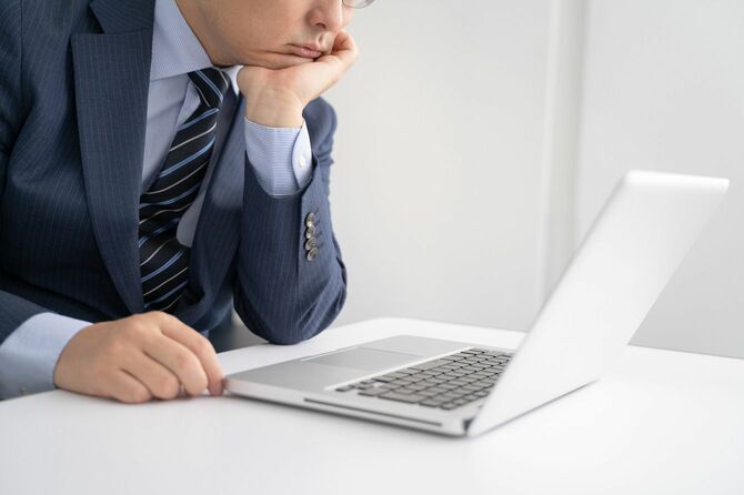 オフィスで頬杖をつきながらノートパソコンを見るビジネスマン