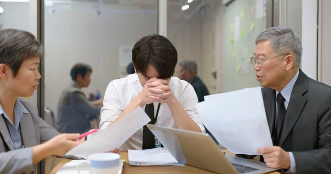 若いビジネスマンを問い詰める二人の中年ビジネスマン