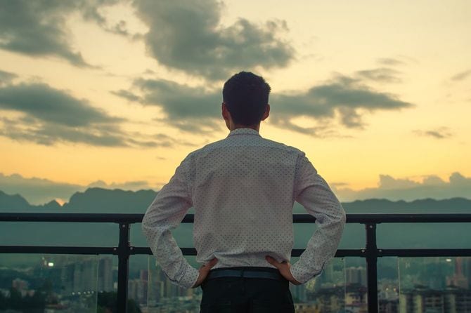 夕日を見て建物の上に立っているビジネスマン