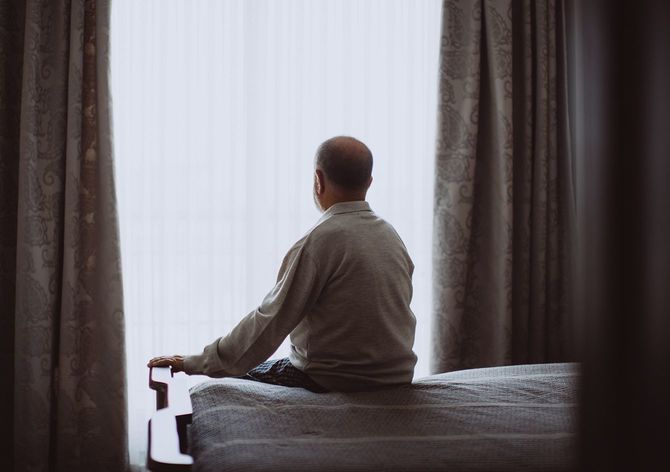 深刻に見えるベッドの上に座っている高齢の男性