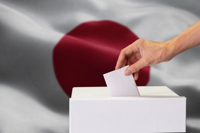 日本国旗を背景に投票箱に用紙を入れる手