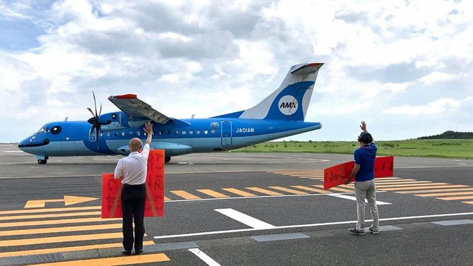 「ご搭乗ありがとうございます」と書かれた手作り看板を掲げ、乗客を見送る